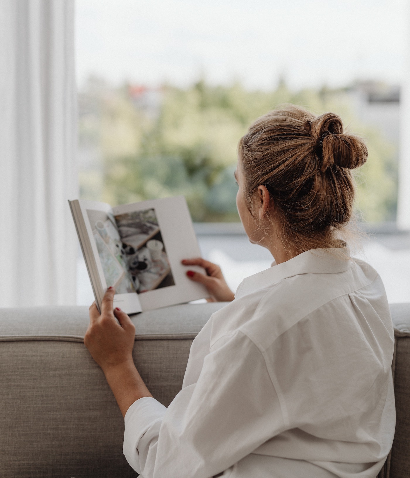 Gemütlich minimalistisch wohnen - Eine Frau sitzt entspannt auf einem Sofa - ihr Lieblingsplatz am Fenster